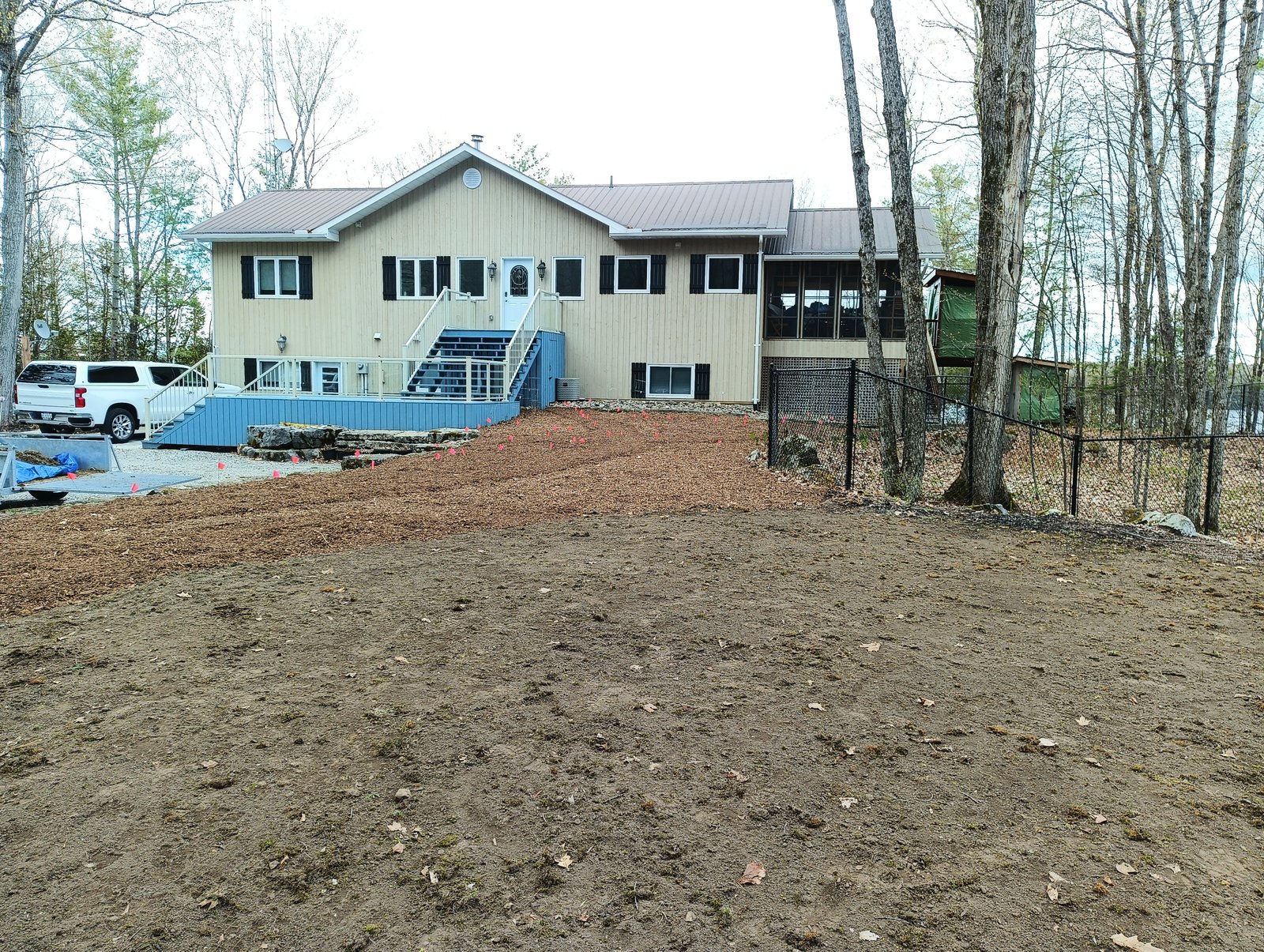 Site ready for installation — mulched house-side garden with the unmulched septic leach bed in the foreground, May 2026